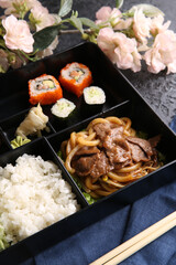 Japanese cuisine. Business lunch in a black box: rice, rolls, salad, sushi on a black table. Background image, copy space