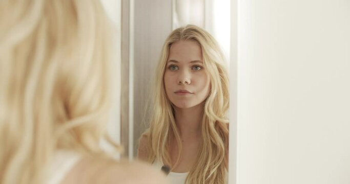 Blonde Woman in Bedroom Facing Mirror with a Makeup Brush