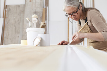 wood crafts, woman artisan carpenter painting with brush and paint jar white the door in workshop, wearing overall and eyeglasses, interior designer, restoration, diy and handmade works concept