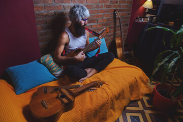 Portrait of bearded man barefoot whit acustic guitar sitting on a bed