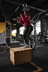 Vertical shot of a sportswoman stepping on the box at the gym