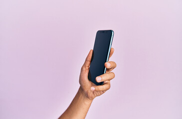 Hand of young hispanic man showing smartphone over isolated pink background.