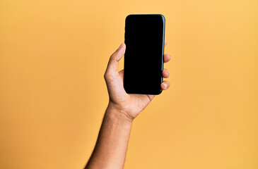 Fototapeta na wymiar Hand of young hispanic man showing smartphone over isolated yellow background.