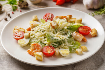 Caesar salad with shrimps  on a large white plate on the table covered with a light linen cloth on a beautiful background of vegetables and herbs. Beautiful bokeh.