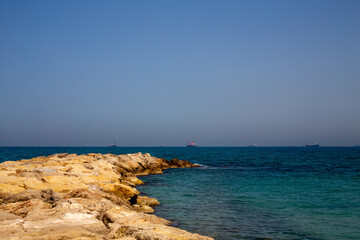 a ridge of yellow stones going into the sea. there are ships in the distance