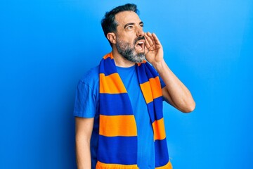 Middle age man with beard and grey hair football hooligan cheering game shouting and screaming loud to side with hand on mouth. communication concept.