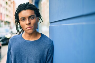 Obraz premium Young african american man with serious expression leaning on the wall at street of city.