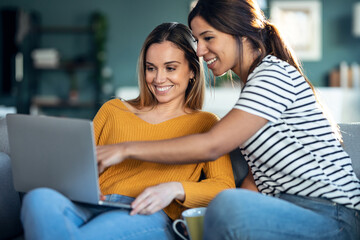 Two happy beautiful women using computer while planning their vacation sitting on the couch at home.