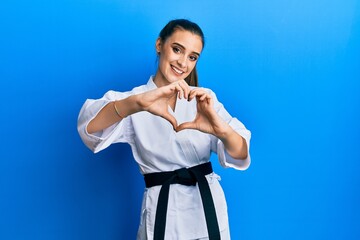 Beautiful brunette young woman wearing karate fighter uniform with black belt smiling in love doing...