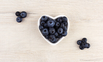 White plate in the shape of a heart with blueberries on a wooden light background