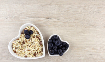 Blueberries and oatmeal in white heart-shaped plates of different sizes on a wooden light background. Healthy breakfast food