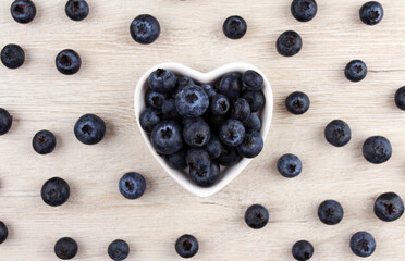 Blueberries in a white plate in the shape of a heart on a wooden background with berries