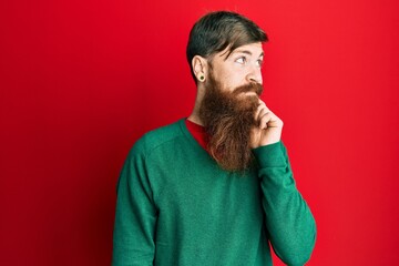 Redhead man with long beard wearing casual clothes thinking concentrated about doubt with finger on chin and looking up wondering