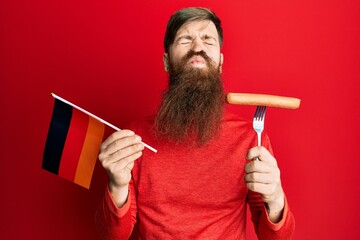 Fototapeta premium Redhead man with long beard holding fork with pork sausage and germany flag looking at the camera blowing a kiss being lovely and sexy. love expression.