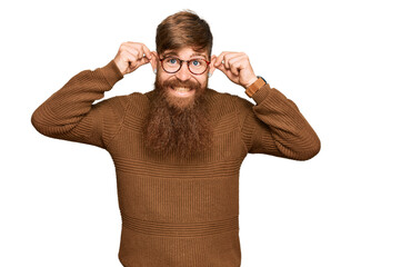 Young irish redhead man wearing casual clothes and glasses smiling pulling ears with fingers, funny...