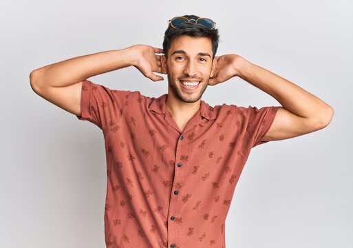 Young handsome man wearing casual summer clothes relaxing and stretching, arms and hands behind head and neck smiling happy