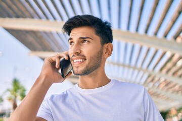 Young latin man smiling happy talking on the smartphone walking at the city.