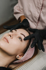 eyebrow microblading. the hands of the master in black gloves hold the maniple on the eyebrow of the model. macro photography