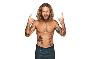 Handsome man with beard and long hair standing shirtless showing tattoos shouting with crazy expression doing rock symbol with hands up. music star. heavy music concept.