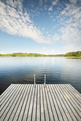 Wooden pier near the river (lake). Evergreen trees in the background. Clear blue sky, reflections...