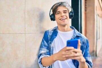 Young hispanic man smiling happy using smartphone and headphones at the city.