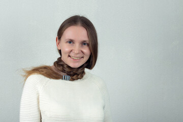Beautiful caucasian young woman with a long braid around her neck on a gray background
