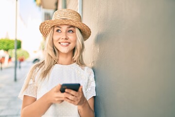 Fototapeta premium Young caucasian tourist girl smiling happy using smartphone at street of city.