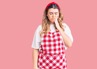 Young caucasian woman wearing apron touching mouth with hand with painful expression because of toothache or dental illness on teeth. dentist