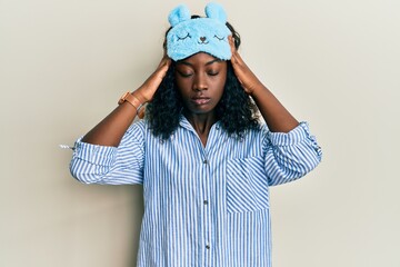 Beautiful african young woman wearing sleep mask and pajama suffering from headache desperate and stressed because pain and migraine. hands on head.