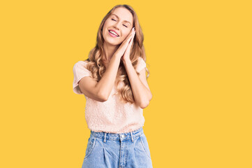 Fototapeta premium Young beautiful caucasian woman with blond hair wearing casual clothes sleeping tired dreaming and posing with hands together while smiling with closed eyes.