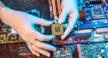 Engineer's gloved hand is holding the CPU chip on the background of the motherboard. High-tech...
