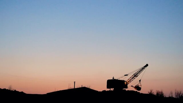 The excavator digs the ground. Mining. Excavator - Silhouette of an excavator loading sand into a truck at sunset. Heavy equipment industry