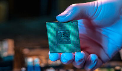 Engineer's gloved hand is holding the CPU chip on the background of the motherboard. High-tech hardware microelectronics