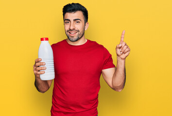 Hispanic man with beard holding liter bottle of milk surprised with an idea or question pointing finger with happy face, number one