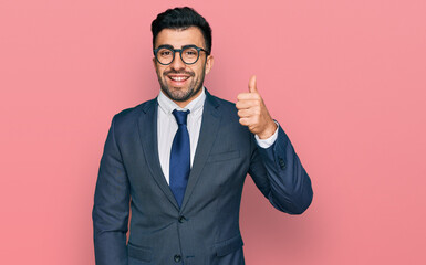 Hispanic man with beard wearing business suit and tie smiling happy and positive, thumb up doing excellent and approval sign