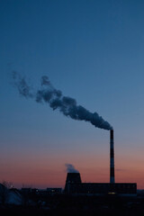 Factory from afar, steam coming from the pipe, industrial zone at sunset