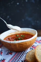 Borscht with sour cream in handmade ceramic bowl on wooden table. Contains bread, green onions, peppers and garlic. Traditional Ukrainian cuisine.