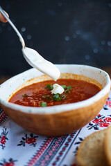 Borscht with sour cream in handmade ceramic bowl on wooden table. Contains bread, green onions, peppers and garlic. Traditional Ukrainian cuisine.