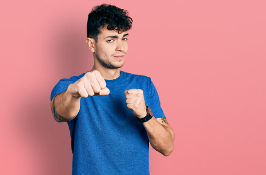 Young hispanic man wearing casual t shirt punching fist to fight, aggressive and angry attack, threat and violence