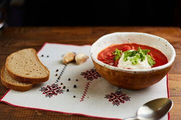 Borscht with sour cream in handmade ceramic bowl on wooden table. Contains bread, green onions, peppers and garlic. Traditional Ukrainian cuisine.