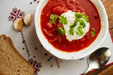 Borscht with sour cream in handmade ceramic bowl on wooden table. Contains bread, green onions, peppers and garlic. Traditional Ukrainian cuisine.