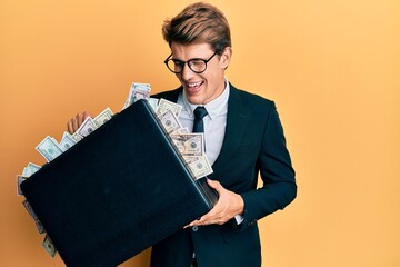 Handsome caucasian business man holding briefcase full of dollars smiling and laughing hard out...