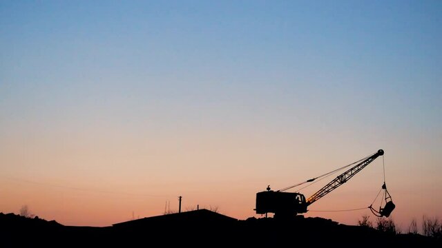 Heavy machinery digging. The excavator digs the ground. Mining. Excavator - Silhouette of an excavator loading sand into a truck at sunset. Heavy equipment industry