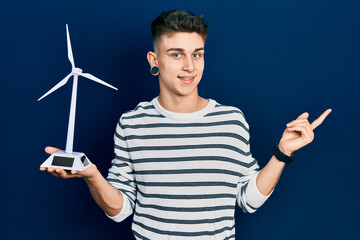Young caucasian boy with ears dilation holding solar windmill for renewable electricity smiling happy pointing with hand and finger to the side