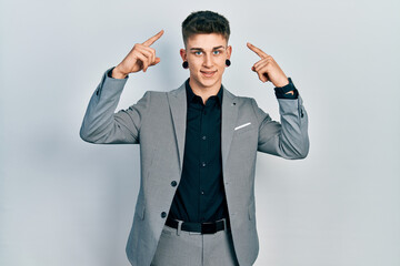 Young caucasian boy with ears dilation wearing business jacket smiling pointing to head with both hands finger, great idea or thought, good memory