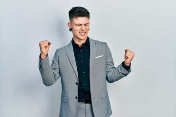 Young caucasian boy with ears dilation wearing business jacket very happy and excited doing winner gesture with arms raised, smiling and screaming for success. celebration concept.