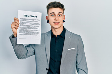 Young caucasian boy with ears dilation holding insurance document looking positive and happy standing and smiling with a confident smile showing teeth