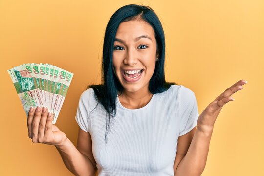 Beautiful hispanic woman holding hong kong 50 dollars banknotes celebrating achievement with happy smile and winner expression with raised hand