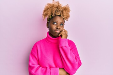 Young african woman with afro hair wearing casual winter sweater thinking concentrated about doubt with finger on chin and looking up wondering