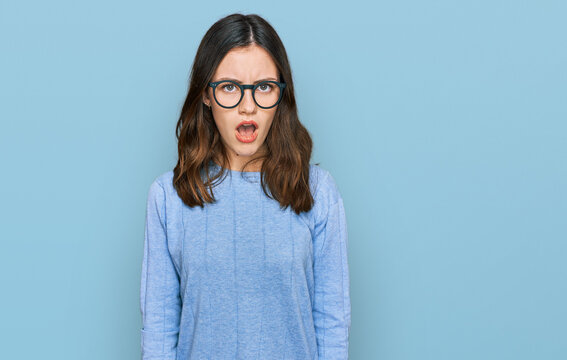 Young beautiful woman wearing casual clothes and glasses in shock face, looking skeptical and sarcastic, surprised with open mouth